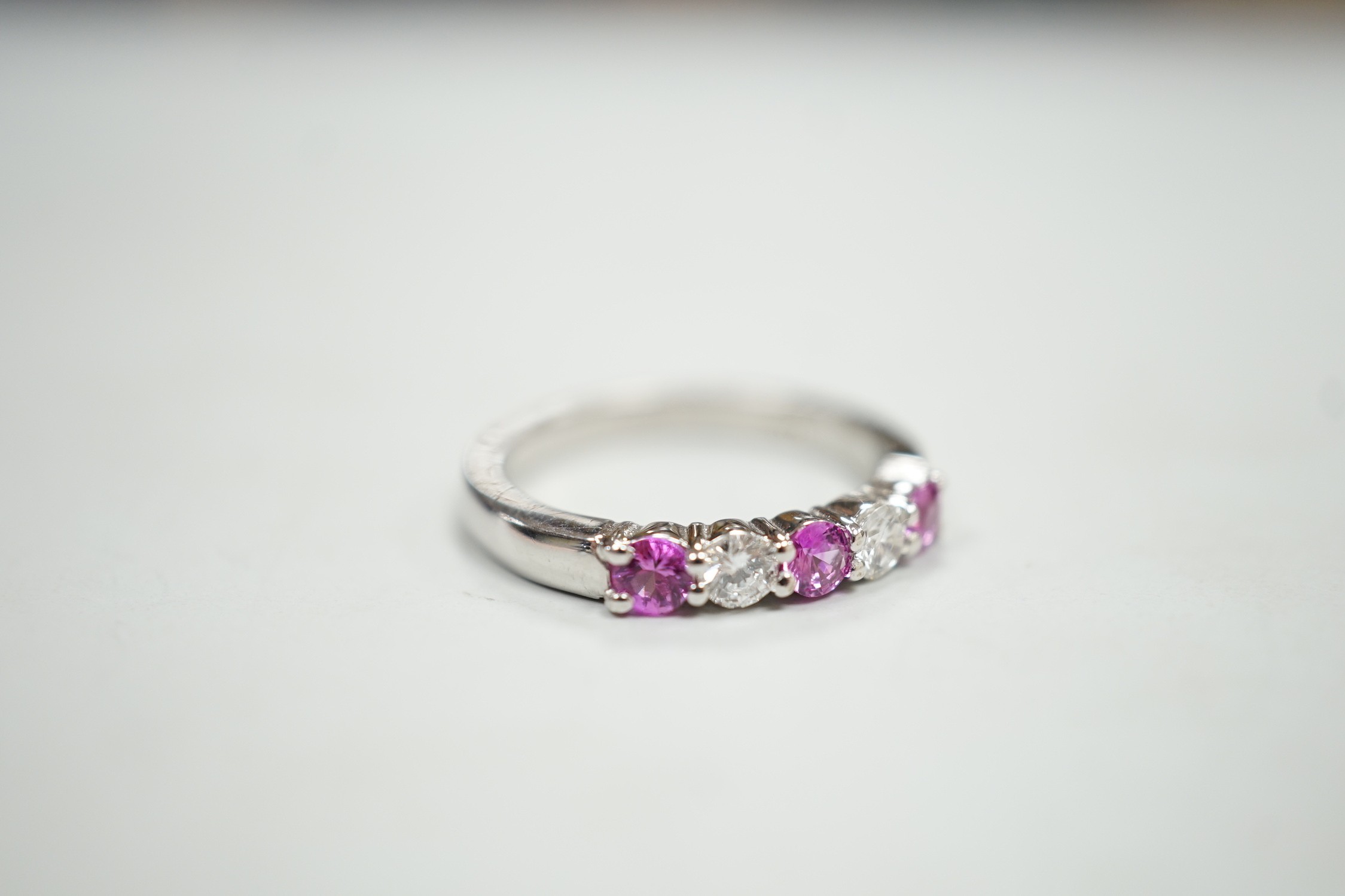 A modern 18ct white gold, three pink stone and two stone diamond set half hoop ring, size M, gross weight 4 grams.